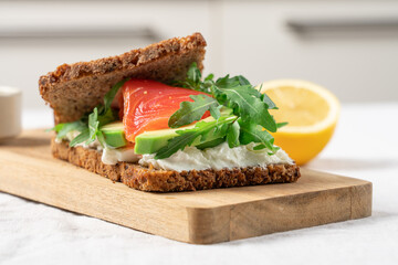 Open sandwich on whole grain bread with smoked salmon, soft cheese, avocado and arugula, healthy gourmet breakfast
