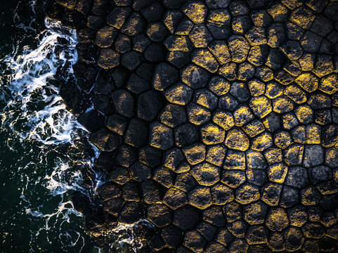 Aerial view of basalt columns kissed by golden sunlight meet the turquoise sea at the stunning Da Dia, Phu Yen, Vietnam.