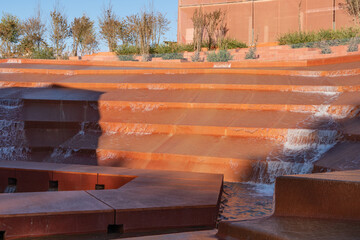 Modern cascading water fountain with terraced red-brown steps, creating serene and visually striking flow of water. Water amphitheater or canyon in Krasnodar's city park, or Galitsky Park.