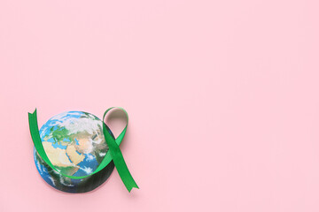 Green ribbon and paper planet Earth on pink background. World Cancer Day