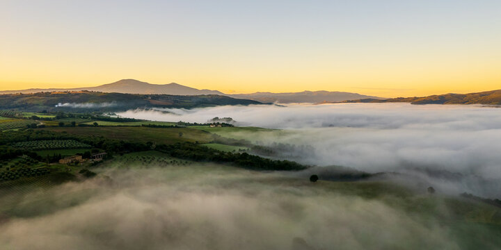 Aerial view of a tranquil morning unveils a sea of fog blanketing the rolling hills and lush valleys of Val dâ€™Orcia, Tuscany, Italy.