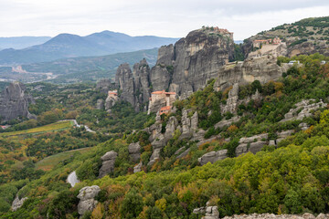 Obraz premium Monasteries crown towering sandstone cliffs in Meteora, surrounded by lush hills and dramatic rock formations.
