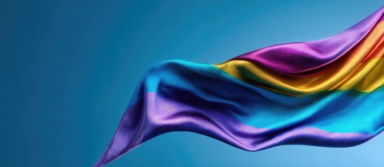 Fototapeta premium Rainbow silk fabric, flowing gently against a bright blue backdrop