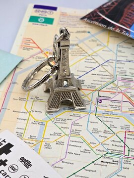 A silvery Eiffel Tower keyring rests on a detailed map of the Paris Metro system, surrounded by tickets and travel documents, symbolizing a city trip. February 13, 2025, Paris, France