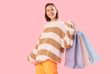 Young woman in warm sweater with shopping bags on pink background