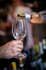 A man's hand holds a glass into which wine is poured