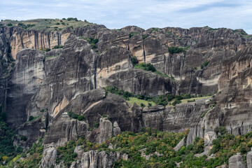 Steep, striated cliffs rise from a rugged landscape in Meteora