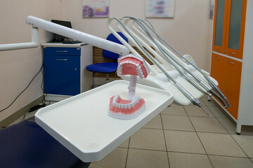 An anatomical model showing the upper and lower jaws with teeth against a background of dental instruments in a dental office.