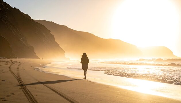 A figure strolls a sunlit beach as ocean waves lap the shore near steep cliffs under a bright sky