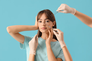 Beautiful young woman before plastic surgery and hands with surgeon's tools on blue background