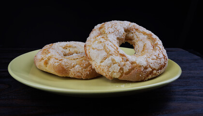 Two ring shaped cupcakes with sugar sprinkles on a yellow plate on a black background.
