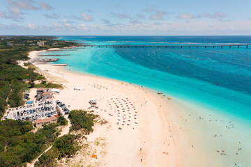 Tourists enjoy a sunny day at a tropical beach with clear blue waters and a long bridge