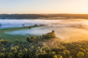 Aerial view of a landscape shrouded in ethereal mist, the sun casting a golden glow over the trees, Henley-on-Thames, Oxfordshire, United Kingdom.