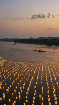 Vertical video: Drifting lanterns glowing down river at dusk, with barge entering and restocking