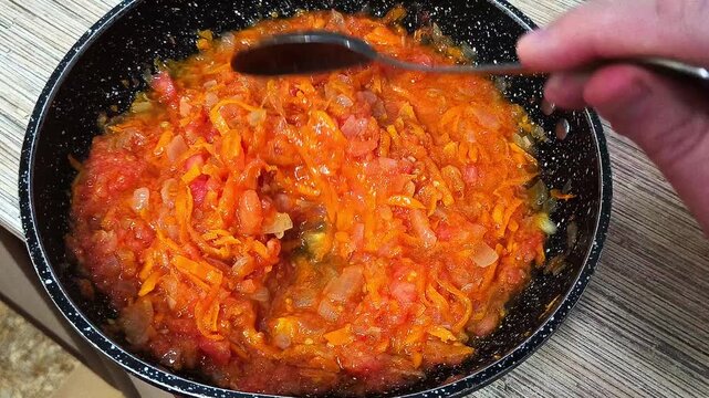 A person stirs stewed vegetables with a spoon. A hand with a spoon stirs food. Stewed vegetables. Sun-dried tomatoes. Tomato paste. Home cooking.