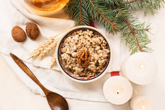 Bowl of traditional Ukrainian Kutya dish with Christmas tree branch and burning candles on white background