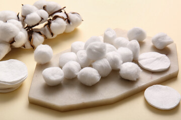 Board with cotton balls, pads and flowers on beige background