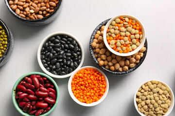 Bowls with different raw legumes on light background