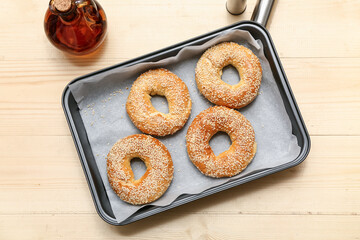 Baking dish of tasty bagels with sesame seeds on wooden background