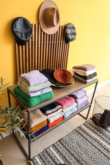 Folded winter sweaters on shelves and folding screen with hats near yellow wall in room