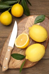 Whole, cut lemons with green leaves and knife on wooden table, flat lay