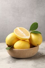 Whole and cut lemons with green leaves in bowl on grey textured table
