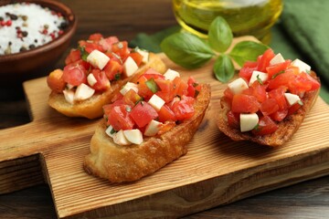 Tasty bruschettas with tomatoes, mozzarella cheese and basil served on wooden table, closeup
