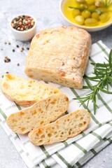 Fresh cut ciabatta, oil, olives, rosemary and peppercorns on grey textured table, closeup