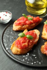 Tasty bruschettas with tomatoes and basil served on black table, closeup