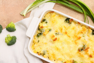 Baking dish with tasty pasta, broccoli and green onion on beige grunge background