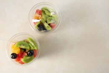 Tasty fruit salad in plastic cups on beige table, flat lay. Space for text