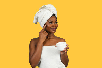 Young black woman applying moisturizer to face