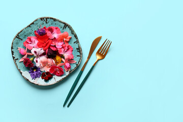 Plate with different beautiful edible flowers and cutlery on blue background
