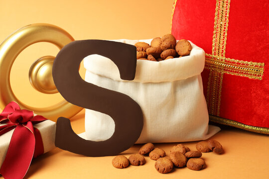 Sinterklaas (Saint Nicholas) Day. Chocolate letter S, kruidnoten cookies, mitre and gift on pale orange background, closeup - Powered by Adobe