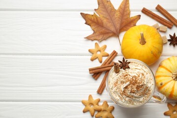 Tasty pumpkin latte with whipped cream in glass cup, cookies and ingredients on white wooden table, flat lay. Space for text