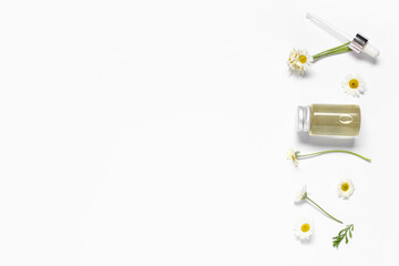 Bottle of chamomile cosmetic oil and flowers on grey background