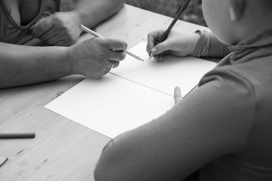 A person guides a child as they write on paper with pens and pencils on a light table in a black and white photo.