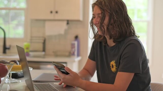 person reviewing resume on device, applicant getting ready for interview in kitchen environment, candidate thoughtfully preparing responses for job interview using multiple devices at home