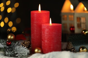 Burning candles, cones, fir tree branches and baubles on light blanket against black background with blurred lights, closeup. Bokeh effect