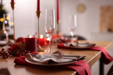 Stylish Christmas table setting with plates, glasses and burning candles in room, closeup. Bokeh effect