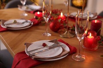 Christmas place setting with festive decor on wooden table in room, closeup