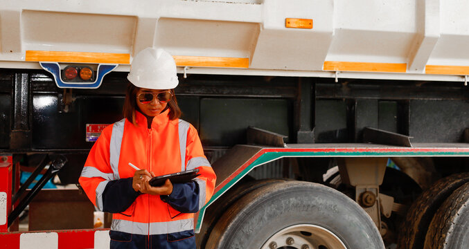 A woman in bright safety gear stands beside a large truck on a construction site, reviewing documents while ensuring proper safety protocols are followed during daytime operations