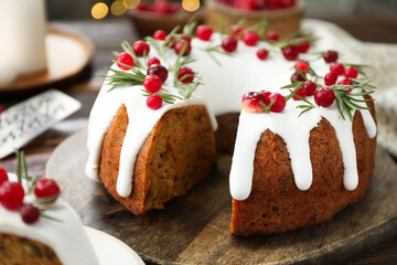 Delicious cut Christmas cake with icing, cranberries and rosemary on wooden table, closeup
