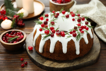 Delicious cut Christmas cake with icing, cranberries and rosemary on wooden table, closeup