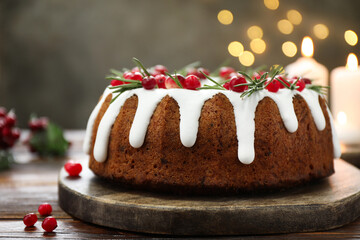 Delicious Christmas cake with icing, cranberries and rosemary on wooden table against grey background with blurred lights, closeup. Bokeh effect