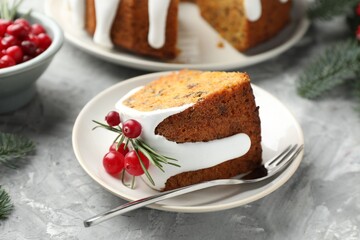 Piece of delicious Christmas cake with icing, cranberries and rosemary on grey textured table, closeup