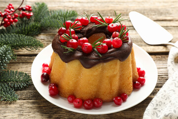 Delicious Christmas cake with chocolate glaze, cranberries, rosemary and fir tree branches on wooden table, closeup