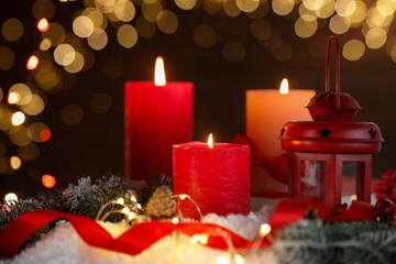 Burning candles and Christmas decor on table against dark background with blurred lights, closeup. Bokeh effect