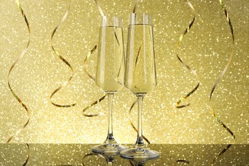 New Year celebration. Sparkling wine in flute glasses and serpentine streamers against shiny golden...