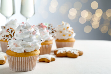 Tasty cupcakes with Christmas decor, gingerbread cookies and champagne on white table, closeup. Space for text